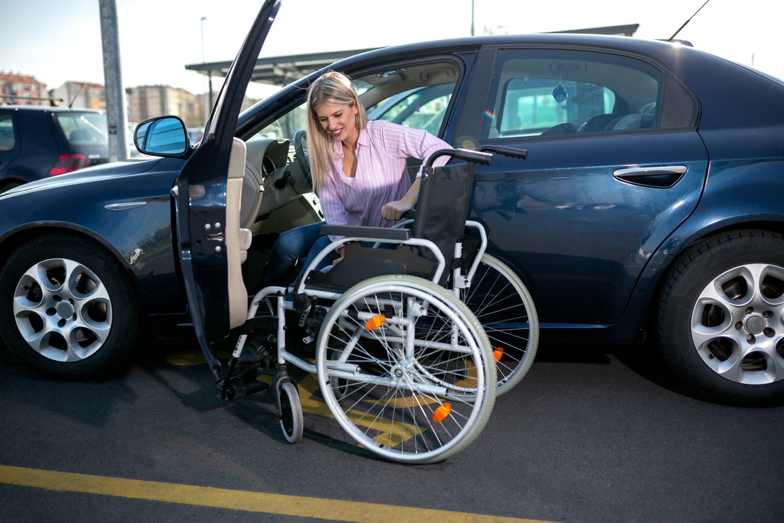Blonde girl with loss of leg function sitting in the car on the parking space for disabled people